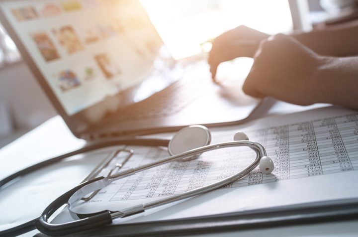 Doctor&rsquo;s stethoscope on documents, laptop in the background.