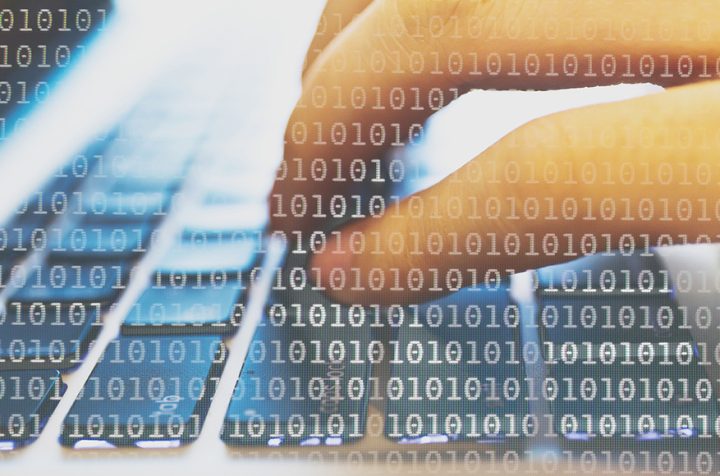 Hand typing on a keyboard with binary code.