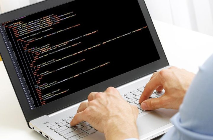 Hands typing on a laptop keyboard with open code.
