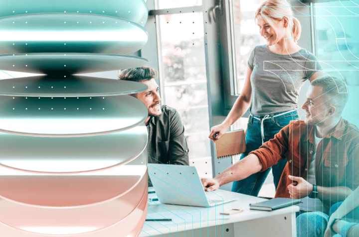 Three people working on a laptop in an office, talking and smiling.