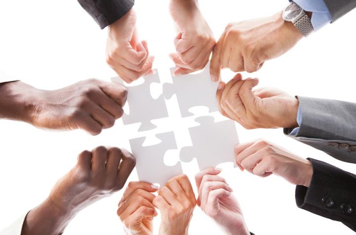 Many people assembling a four-piece puzzle – teamwork and collaboration.