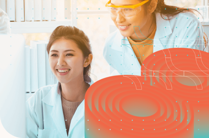 Two happy women in lab coats looking at a computer.