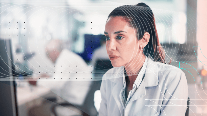 Woman in a white lab coat working at a computer, depicting remote research.