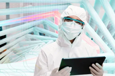A technician in protective clothing and a mask holding a tablet in the laboratory.