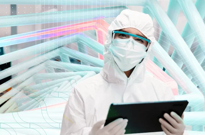 A technician in protective clothing and a mask holding a tablet in the laboratory.