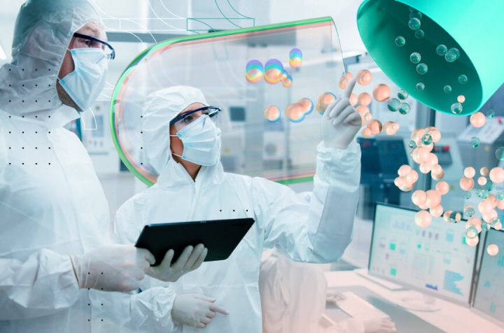 Pharma professionals in cleanroom suits with tablet and 3D molecular hologram.